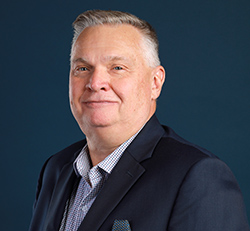 Older white male with short gray hair, wearing a navy blue blazer