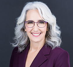 White female with gray/white hair in a purple blazer